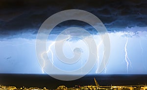 Massive cloud to ground lightning bolts hitting the horizon of city lights