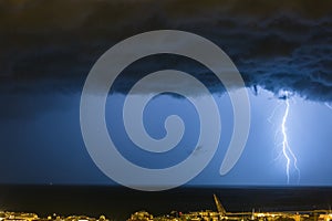 Massive cloud to ground lightning bolts hitting the horizon of city lights