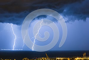 Massive cloud to ground lightning bolts hitting the horizon of city lights