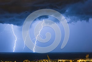 Massive cloud to ground lightning bolts hitting the horizon of city lights