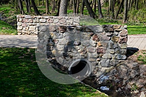 Massive construction of a small bridge over a stream where there is drainage by a concrete pipe. The railing is made of stone from