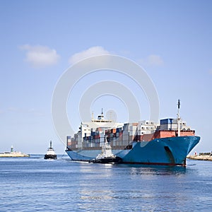 Massive Container Ship Entering River Mouth Assisted by Two Tugs