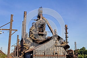 Massive industrial complex, abandoned and weathered furnaces and smokestacks before a deep blue sky