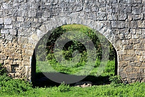 Massive old stone arch under stone bridge allowing access to local field surrounded with uncut grass