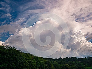 Massive rain cloud, Cumulus congestus, in the blue sky over wooded hill