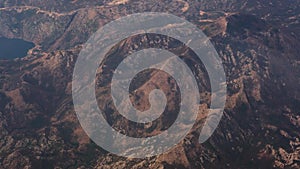 Massive rocky mountain summit peak sharp jagged cliff edge wide shot aerial, distant view out of the jet-plane window