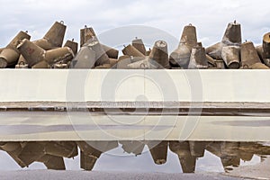 Massive stack of breakwater with reflection in rain puddle