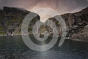 Massive structured steep stone wall with green moss and water