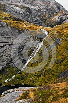 Massive structured steep stone wall with green moss and water at the bottom in the mountains on the Lofoten Islands in Norway