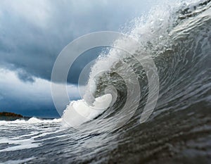 A massive wave crashes in the water on a cloudy day, stirred up by the wind