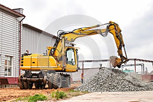 A massive yellow construction excavator stands parked in front of a building, showcasing its heavy-duty equipment against the