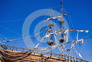 mast with sails on an ancient wooden pirate ship against background of blue sky in ocean