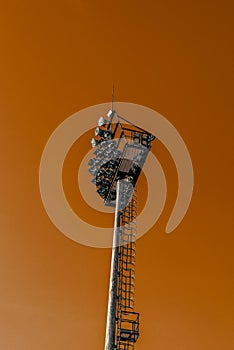 Mast with spotlights illuminate on stadium and orange sky background