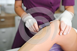 A master applies depilatory wax to a young woman& x27;s leg for hair removal. Depilation with wax. Beauty concept. Place