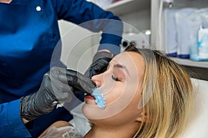 master applying cosmetics gel wax upper lip before hair removal procedure in clinic