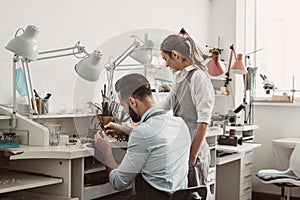 Master and apprentice. Young male assistant and female jeweler are working together at jewelry making workshop.