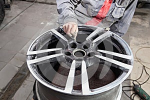 Master body repair man is working on preparing the surface of the aluminum wheel of the car for subsequent painting in the