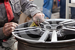 Master body repair man is working on preparing the surface of the aluminum wheel of the car for subsequent painting in the