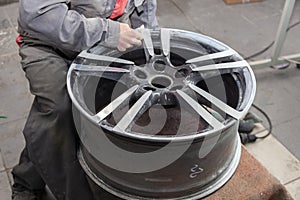 Master body repair man is working on preparing the surface of the aluminum wheel of the car for subsequent painting in the