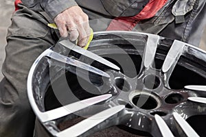 Master body repair man is working on preparing the surface of the aluminum wheel of the car for subsequent painting in the photo