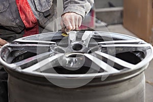 Master body repair man is working on preparing the surface of the aluminum wheel of the car for subsequent painting in the