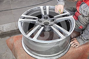 Master body repair man is working on preparing the surface of the aluminum wheel of the car for subsequent painting in the