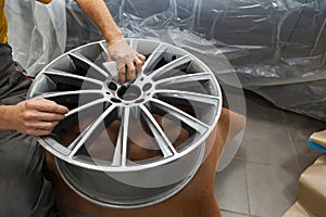 Master body repair man is working on preparing the surface of the aluminum wheel of the car for subsequent painting in the photo