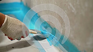 A worker is applying waterproofing paint to the floor in the bathroom. The master with a brush applies a protective photo