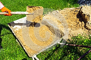 A master builder shovels sand into a cart to prepare concrete. Close-up of a master hand during construction work photo