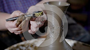 Master of ceramic production is decorating fresh clay bowl by ornament in a shop, using rotating wheel with patterns