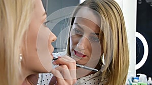 Master cosmetologist tints the contours of the lips of a female client.