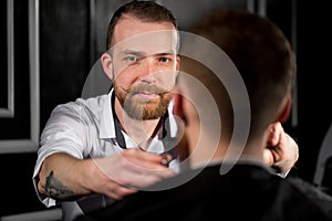 Master cuts hair and beard in the Barber shop. Hairdresser makes hairstyle using scissors and a metal comb.