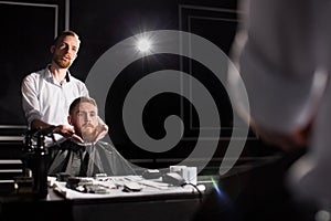 Master cuts hair and beard in the Barber shop. Hairdresser makes hairstyle using scissors and a metal comb.