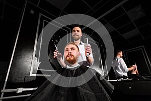 Master cuts hair and beard in the Barber shop. Hairdresser makes hairstyle using scissors and a metal comb.