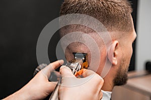 Master cuts man hair using comb and trimmer in barbershop