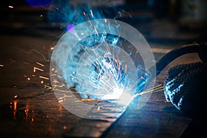Master is doing welding at his workplace in the workshop, while sparks are flying all around, they are wearing a protective helmet