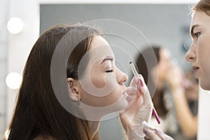 The master dyes the eyebrows brown to a beautiful young Caucasian girl. Close-up.