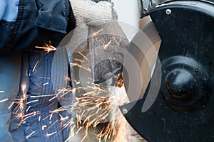 master in gloves and blue jacket sharpens axe on electric sharpener outdoors. Process of sharpening blunt tool with sparks flying