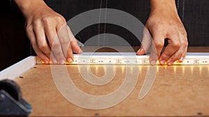 The master glues the LED strip into the niche of the shelf from the cabinet for lighting.installation of diode lighting tape