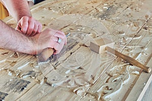 Master hands cut a pattern on a large wooden Board. Creation of carved patterns for furniture and household items. Work on the