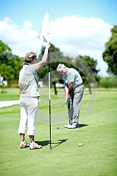 Master of the hole-in-one. A senior woman holding a flag while her husband puts for birdie.