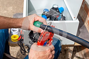 The master installs drip irrigation for the garden. A man cuts off a HDPE pipe with a pipe cutter