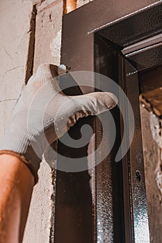 The master installs the front door with a metal box to them, inserts white plugs into the door frame, close-up