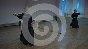 Master kendoka performs kata in the sports hall with mirrors, makes the fall with the katan sword