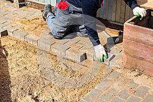 The master in lays paving stones in layers. Garden brick pathway paving by professional paver worker. Laying gray concrete paving