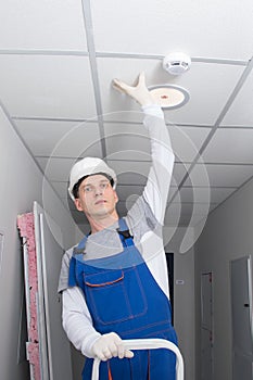 A master from the management company, wearing a hard hat and a professional uniform, was replacing a light bulb and checking the
