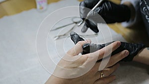 Master of manicure in black gloves, paints manicure for a woman in a beauty salon. Top view.