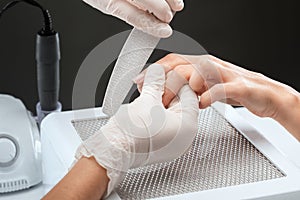 The master of the manicure saws and attaches a nail shape during the procedure of nail extensions in the beauty salon.