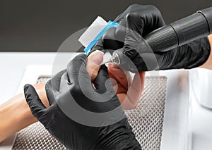 The master of the manicure saws and attaches a nail shape during the procedure of nail extensions in the beauty salon.