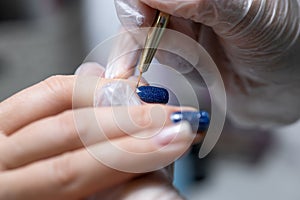 The master of the nail service makes a manicure by distributing gel polish on the surface of the nail with a thin nail brush